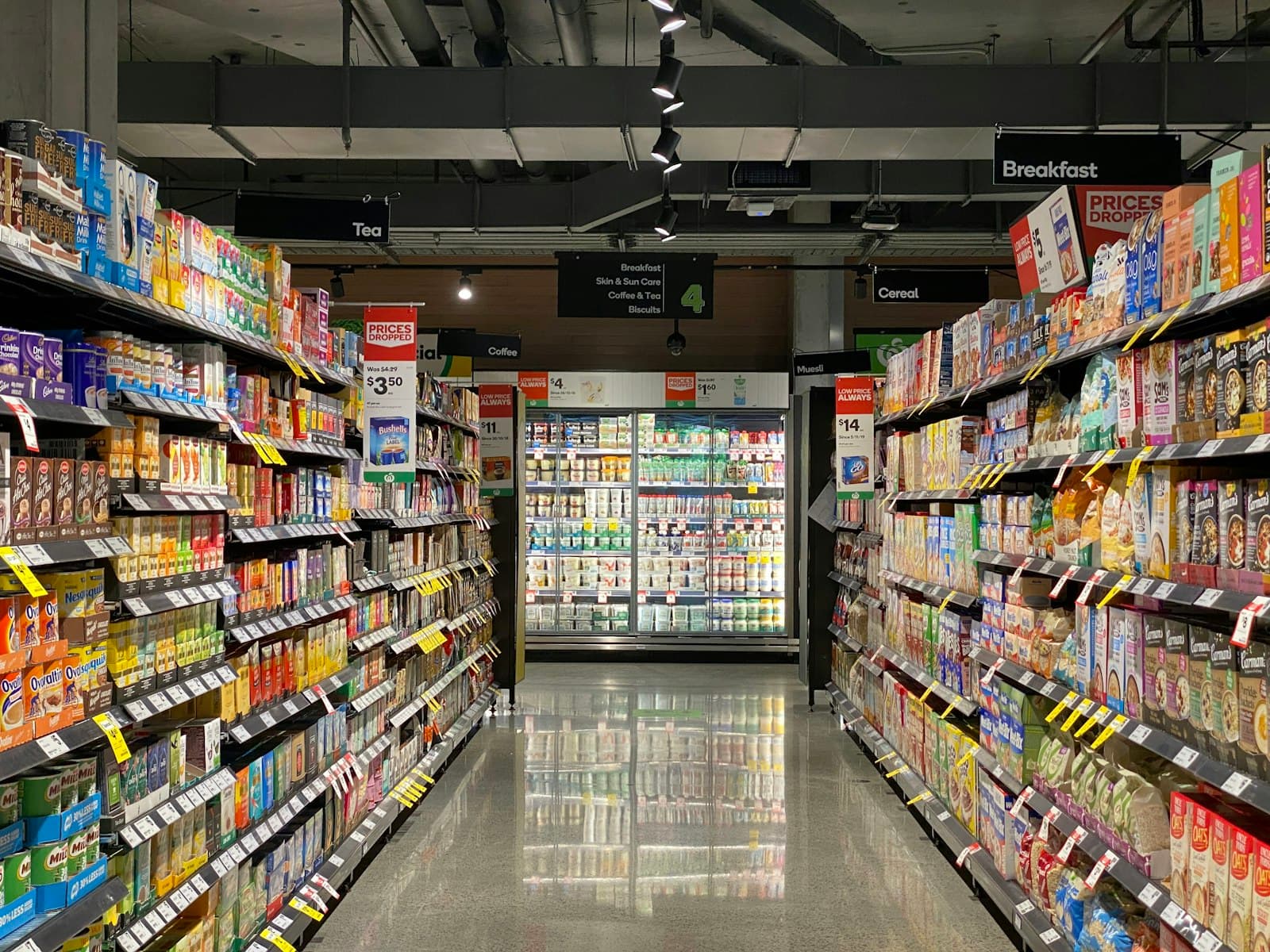 A supermarket aisle with stocked shelves under hanging signage