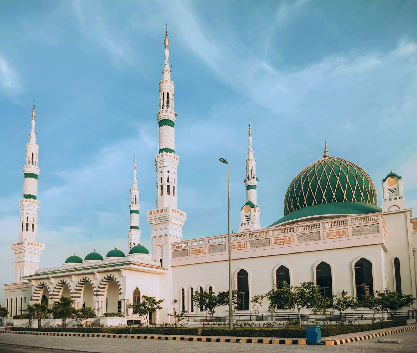 A white mosque with a green dome and minarets under a clear sky