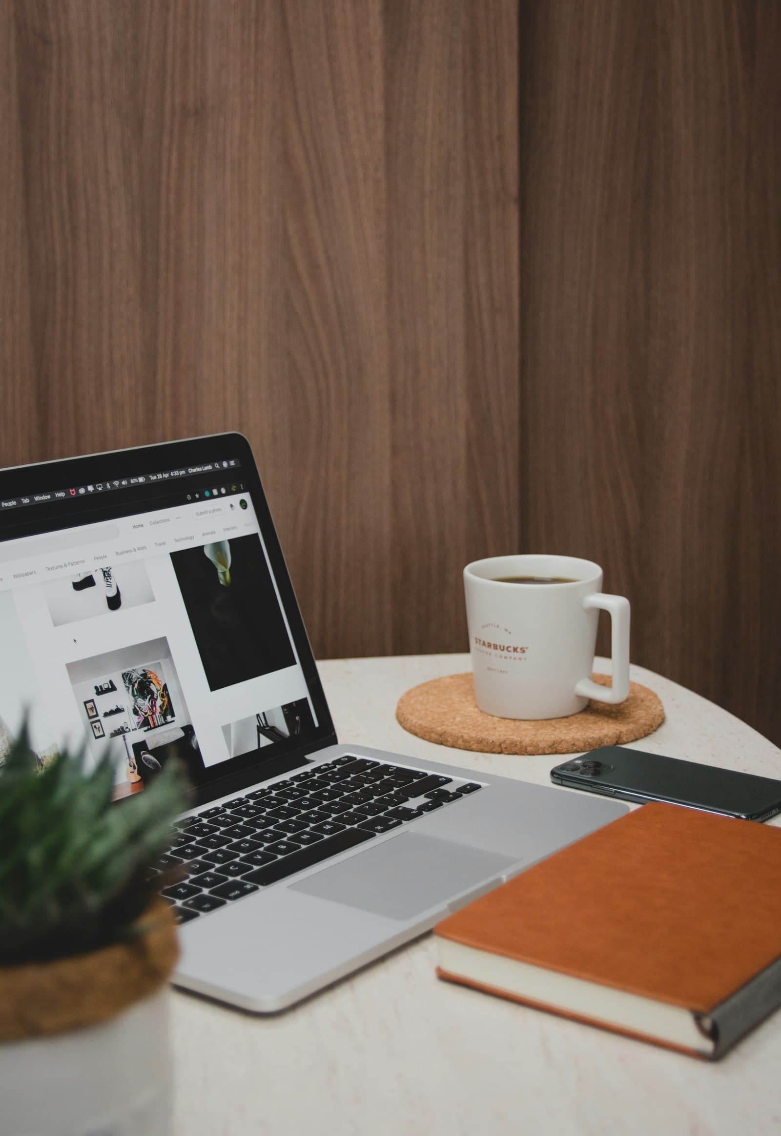 A laptop, leather notebook and coffee on a small wooden table